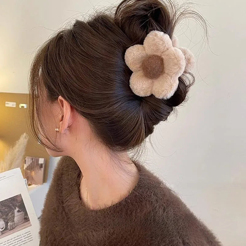 Woman with brown hair styled in an updo with a decorative flower hair accessory, wearing a brown sweater.