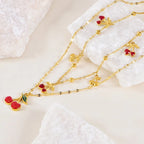 Gold necklace with cherry and leaf charms on a textured white surface