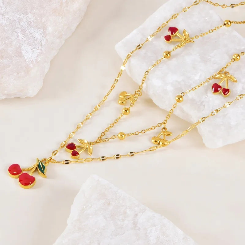 Gold necklace with cherry and leaf charms on a textured white surface