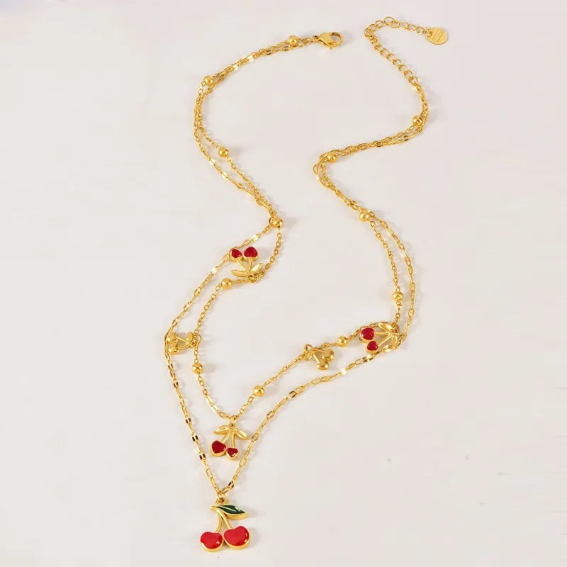 Gold necklace with cherry pendants on a light pink background
