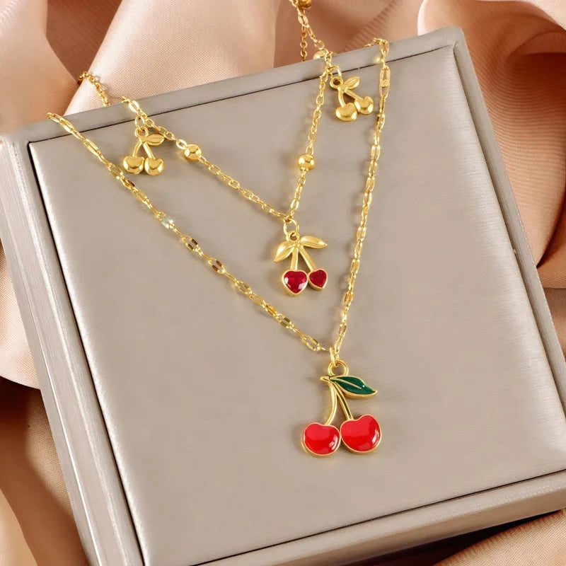 Gold necklace with cherry pendants on a beige surface