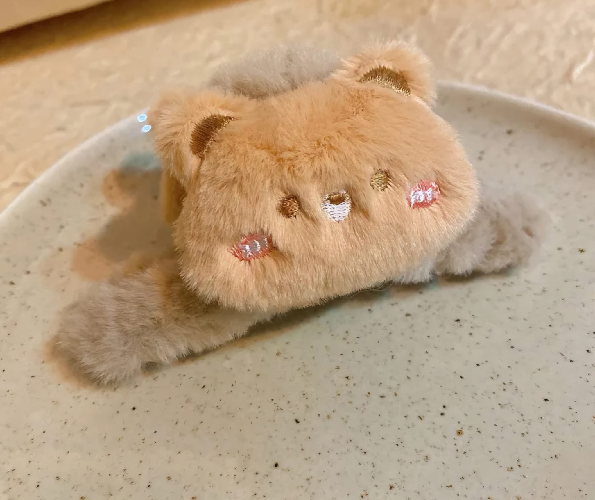 Fluffy beige cat-shaped clip with decorative elements on a textured surface
