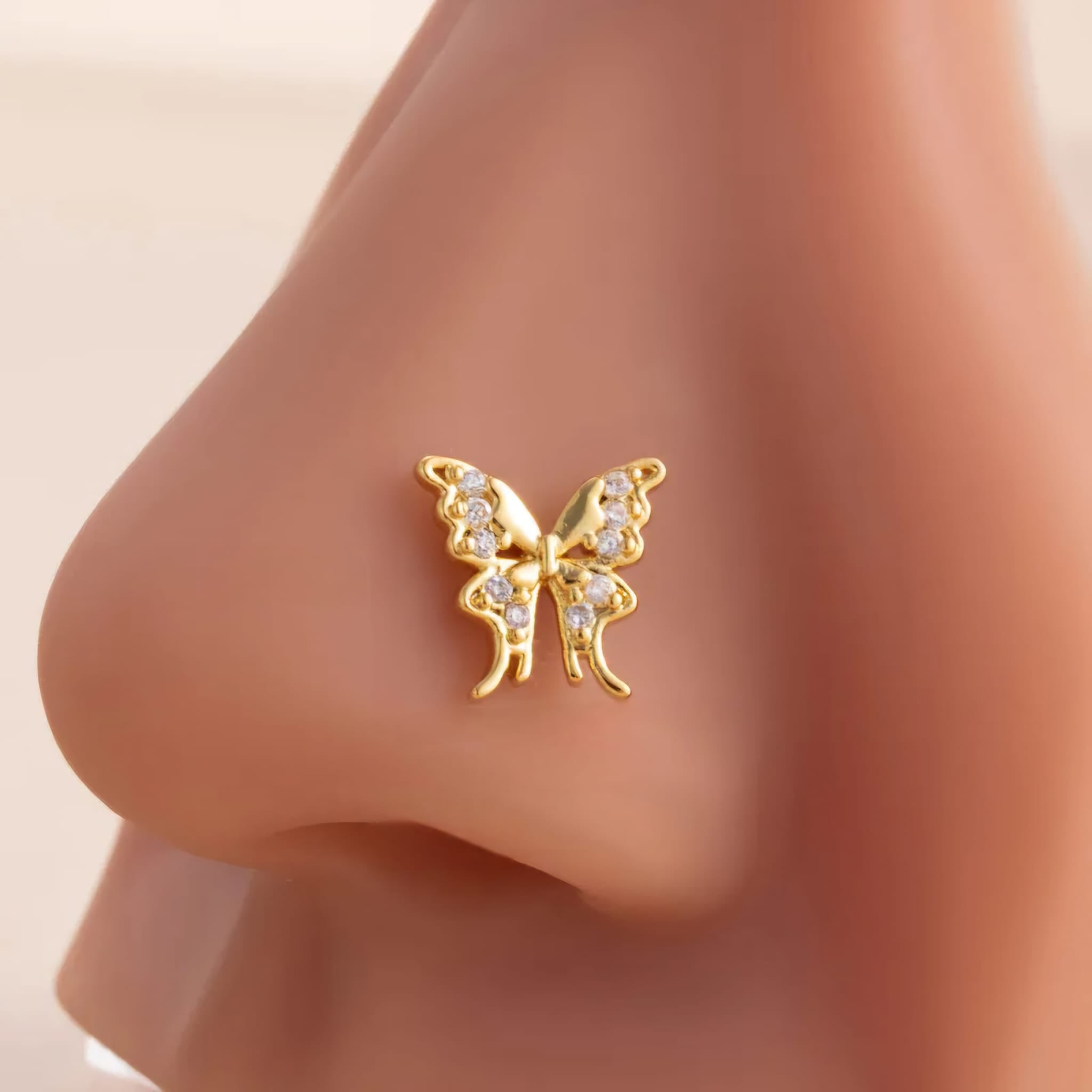 Gold butterfly nose ring on a person's nose with a neutral background