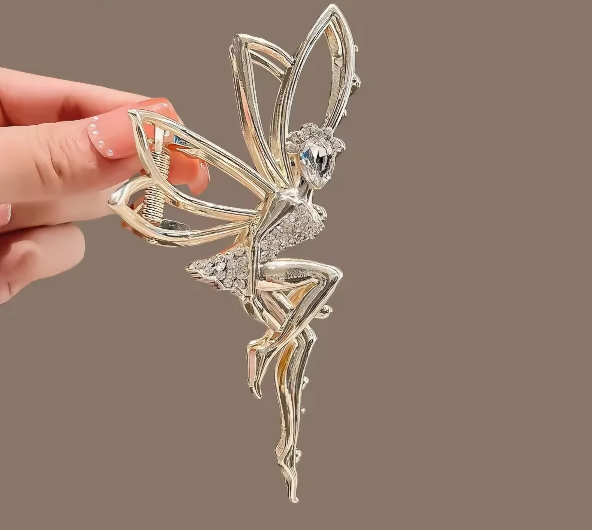 Silver fairy clip held by a hand against a brown background