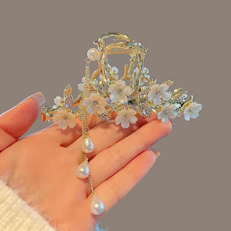 Decorative hair clip with floral and pearl details held by a hand against a neutral background