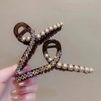 Decorative hair clip with pearls and crystals held by a hand against a neutral background