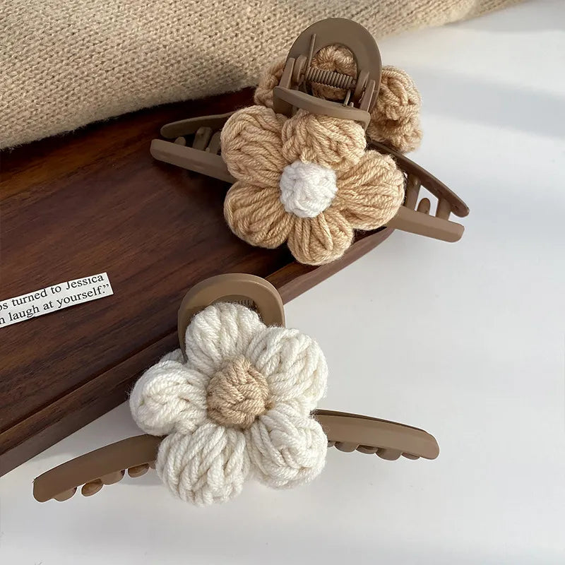 Two knitted flower hair clips on a wooden tray with a white background