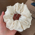 White lace scrunchie held in a hand with a blurred background