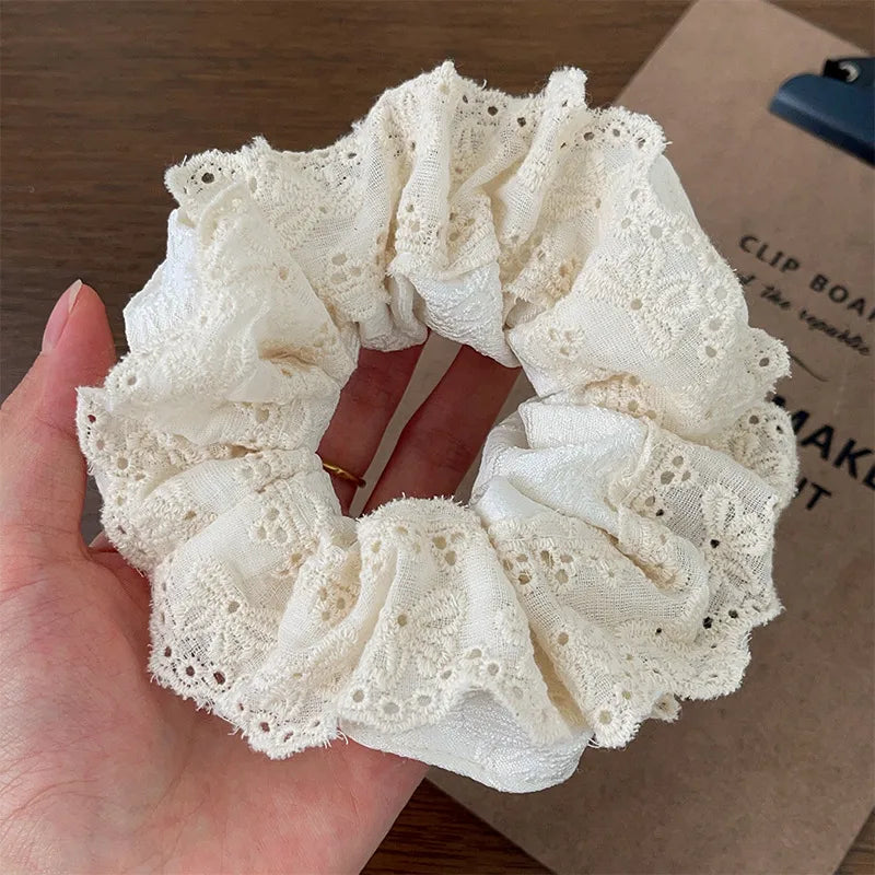 White lace scrunchie held in a hand with a blurred background